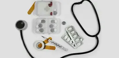 A stethoscope, pill packets, and other medical tools scattered on a white surface.