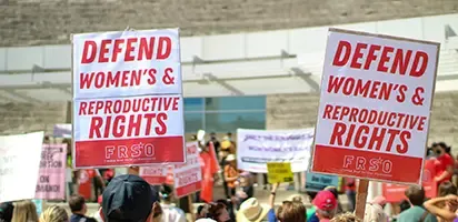 A crowd of protesters holding signs that read: "Defend Women's and Reproductive Rights".