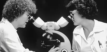 Two women looking into microscopes in a black and white photo.