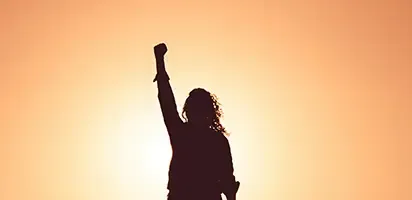 Silhouette of a woman, her right arm is raised with a clenched fist.