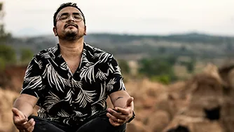 A man sitting cross-legged on a rock, meditating.